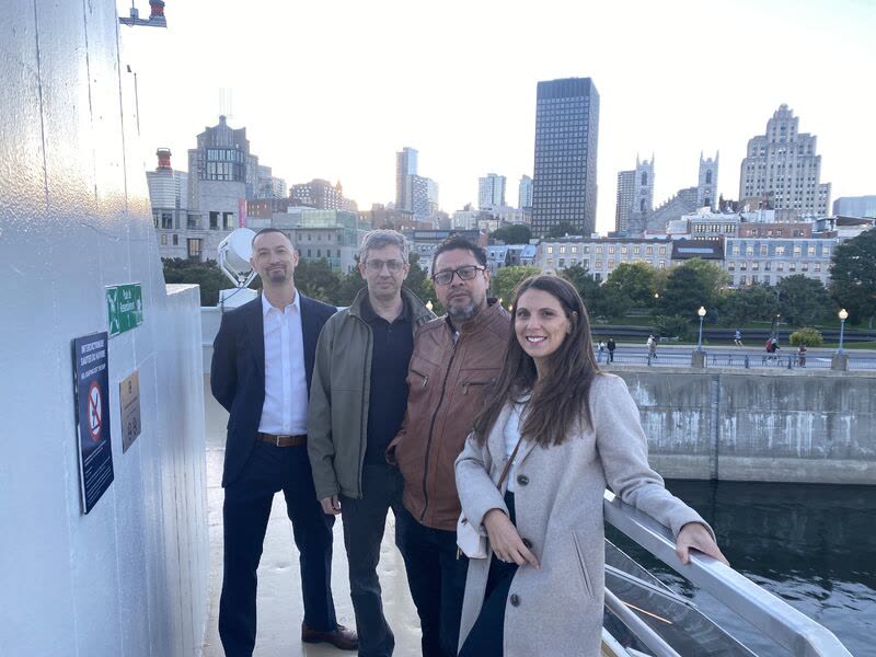 Four team members on the boat deck, with Montreal's Old Port and skyline behind them
